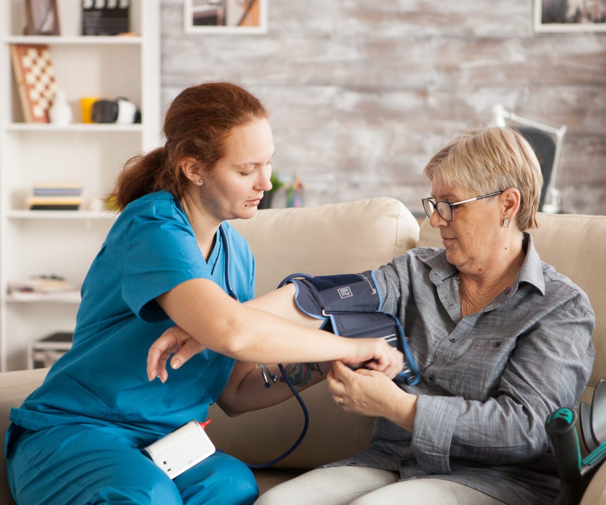 Female nurse using digital blood pressure device on senior woman in nursing home.